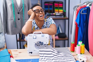 African american woman tailor smiling confident leaning on sewing machine at tailor shop