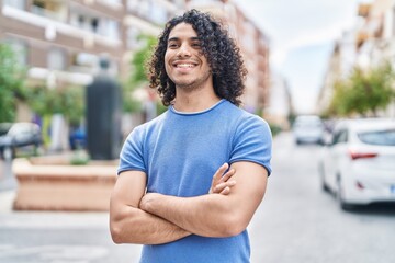 Young latin man standing with arms crossed gesture at street
