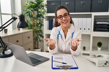 Young hispanic woman wearing doctor uniform and stethoscope smiling cheerful offering hands giving assistance and acceptance.