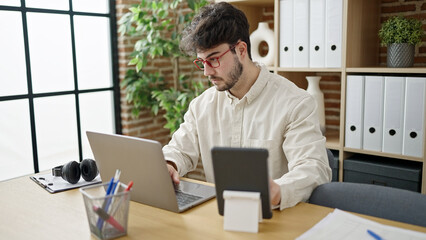 Young hispanic man business worker using touchpad and laptop at office