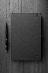 Vista superior de um caderno fechado com uma lapiseira ao lado em fundo de madeira em preto e...