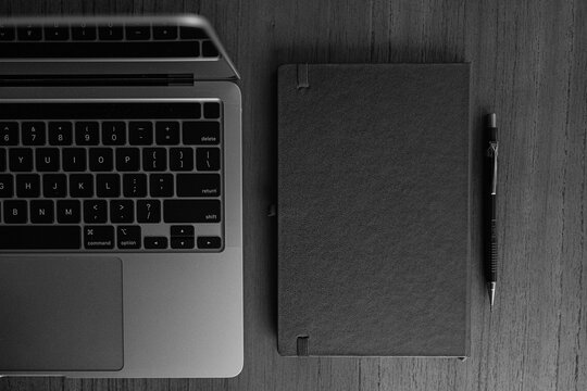 fotografia superior em preto e branco computador aberto ao lado de bloco de notas sobre mesa com espa&ccedil;o livre para texto
