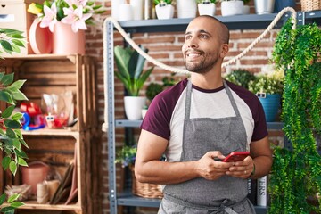 Young latin man florist smiling confident using smartphone at flower shop