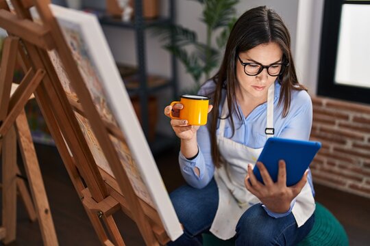 Young woman artist drinking coffee using touchpad at art studio