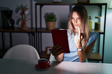 Young hispanic woman using touchpad sitting on the table at night showing middle finger, impolite...