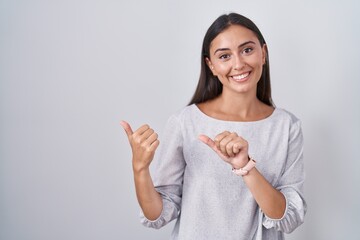 Young hispanic woman standing over white background pointing to the back behind with hand and...