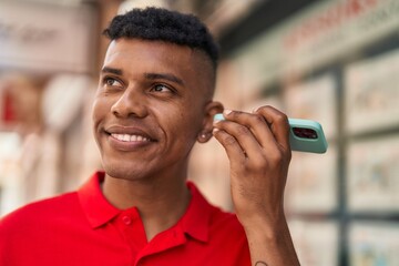 Young latin man smiling confident listening audio message by the smartphone at street