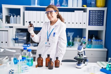 Young beautiful hispanic woman scientist holding bottle at laboratory