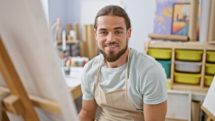 Fototapeta na wymiar Young hispanic man artist smiling confident sitting on chair at art studio