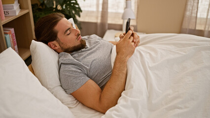 Obraz na płótnie Canvas Young hispanic man using smartphone lying on bed at bedroom