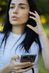 Young woman in casual clothes while relaxing in the public park and holds smartphone in her hands and scrolls through the news feed. Close-up shot of gerl and her hands with phone