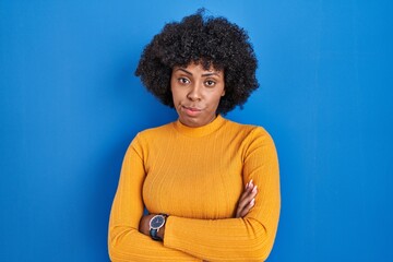 Fototapeta na wymiar Black woman with curly hair standing over blue background skeptic and nervous, disapproving expression on face with crossed arms. negative person.
