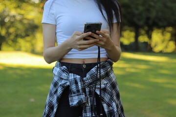 Young woman in casual clothes while relaxing in the public park and holds smartphone in her hands and scrolls through the news feed. Close-up shot of gerl and her hands with phone