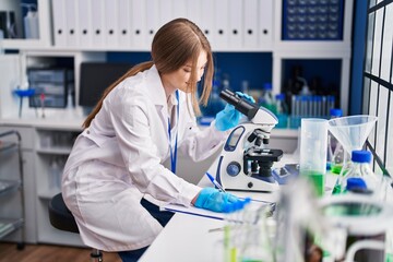 Young caucasian woman scientist using microscope write on document at laboratory