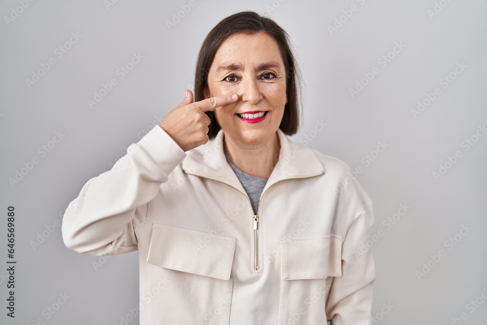 Wall mural middle age hispanic woman standing over isolated background pointing with hand finger to face and no