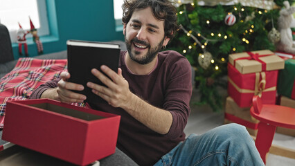 Young hispanic man smiling confident unpacking book of christmas gift at home