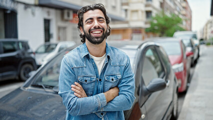 Young hispanic man smiling confident standing by car with arms crossed gesture at street