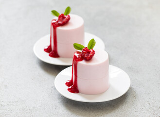 Raspberry cream jelly pudding, Panna Cotta cylindrical shape, with raspberry topping. On a plate. Light gray background. Close-up