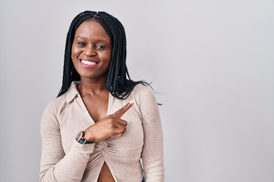 African woman with braids standing over white background cheerful with a smile on face pointing with hand and finger up to the side with happy and natural expression