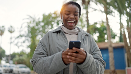 African american woman using smartphone smiling at street