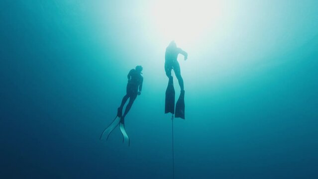Male freediver ascending along the rope during free diving work out in the open sea with his safety buddy