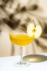 Apple pie cocktail drink with vodka, apple liqueur and cinnamon syrup.. Light beige background, hard light, shadow pattern