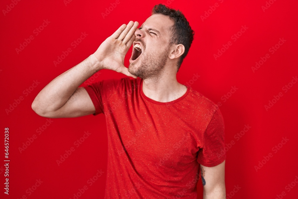 Canvas Prints Young hispanic man standing over red background shouting and screaming loud to side with hand on mouth. communication concept.