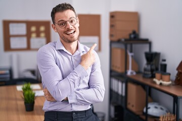 Fototapeta premium Young hispanic man at the office with a big smile on face, pointing with hand finger to the side looking at the camera.
