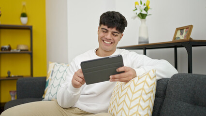 Young hispanic man using touchpad sitting on sofa at home