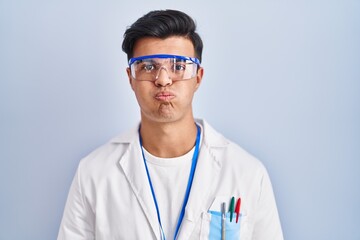 Hispanic man working as scientist puffing cheeks with funny face. mouth inflated with air, crazy expression.