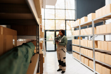 Selective focus of shelves full with packages ready for delivery, in background stockroom supervisor talking at landline phone with remote manager. African american worker preparing customers orders