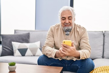 Middle age grey-haired man using smartphone sitting on sofa at home