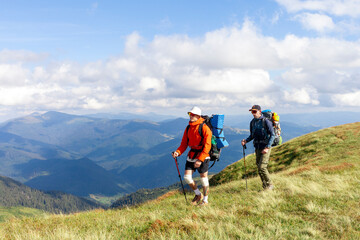 two men with hiking equipment and backpacks go to the mountains with trekking poles