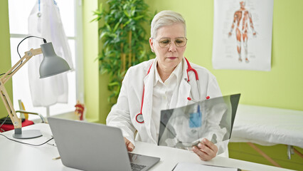 Middle age grey-haired woman doctor looking at xray using laptop at clinic