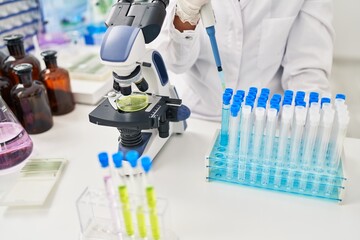 Young beautiful hispanic woman scientist pouring liquid on test tube at laboratory