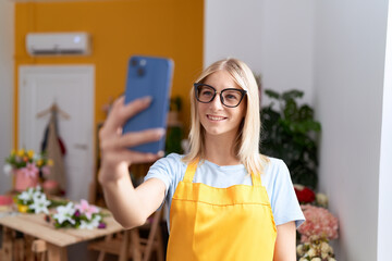 Young blonde woman florist make selfie by smartphone at flower shop