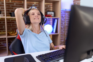 Young caucasian woman playing video games wearing headphones smiling confident touching hair with hand up gesture, posing attractive and fashionable