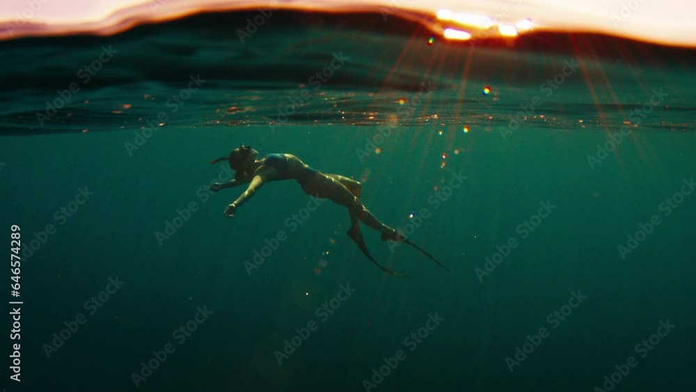 Poster woman freediver swims underwater in the sea at sunset and relaxes and floats beneath the surface