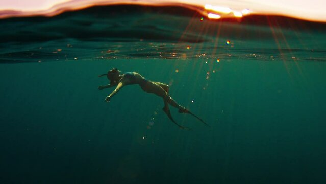 Woman freediver swims underwater in the sea at sunset and relaxes and floats beneath the surface