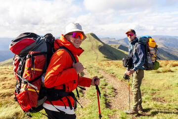 two men with hiking equipment and backpacks go to the mountains with trekking poles