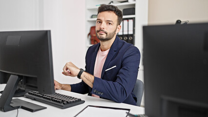 Young hispanic man business worker using computer looking watch at office