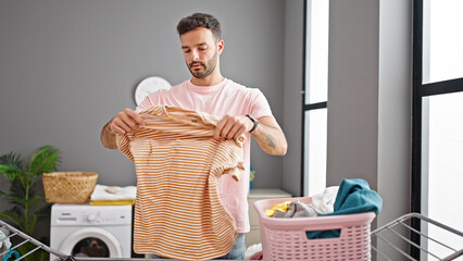 Young hispanic man hanging clothes on clothesline at laundry room