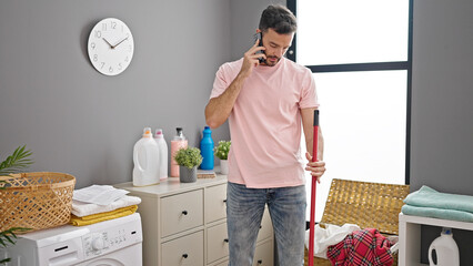 Young hispanic man using smartphone washing clothes at laundry room