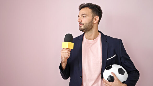 Young hispanic man soccer reporter doing interview speaking over isolated pink background