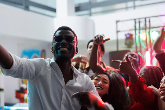 Cheerful happy friends taking selfie while partying together in nightclub. Diverse young carefree people looking at smartphone camera while making photo on club dancefloor