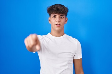 Hispanic teenager standing over blue background pointing displeased and frustrated to the camera,...