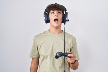 Hispanic teenager playing video game holding controller angry and mad screaming frustrated and furious, shouting with anger. rage and aggressive concept.