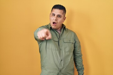 Hispanic young man standing over yellow background pointing displeased and frustrated to the camera, angry and furious with you