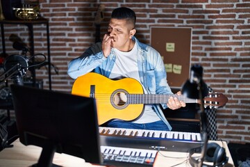 Hispanic young man playing classic guitar at music studio looking stressed and nervous with hands...