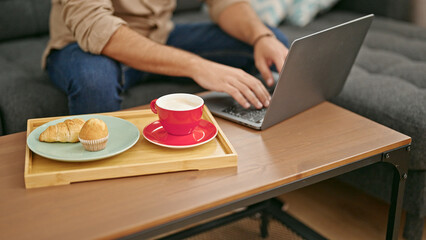 Young hispanic man typing on laptop at home